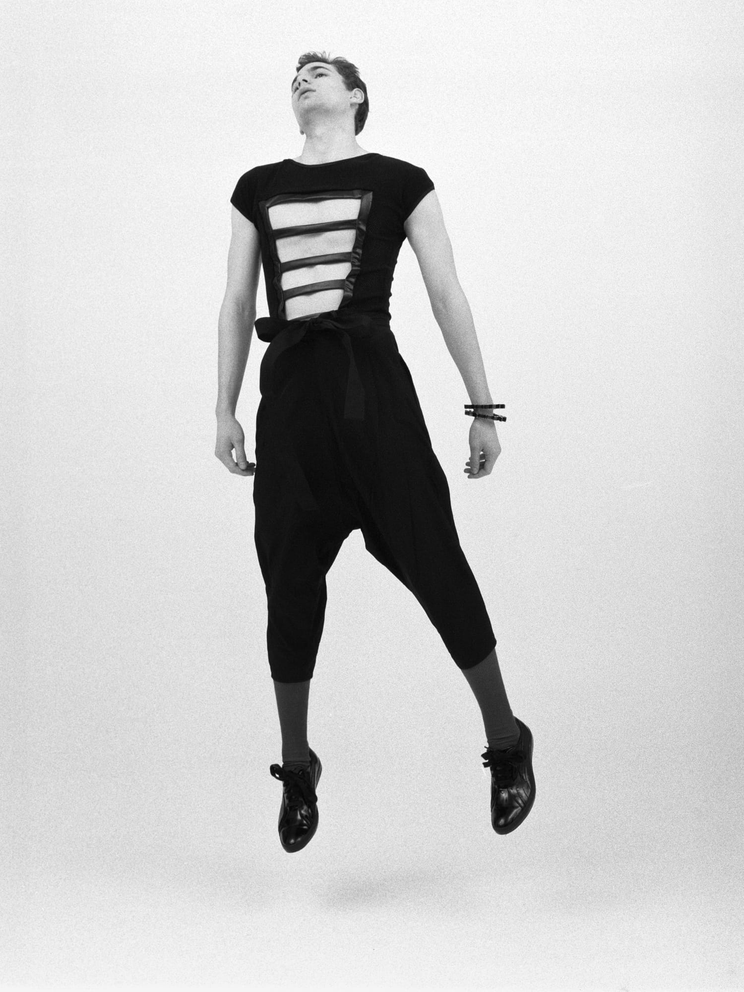 Man jumping in the air, wearing an all black outfit with horizontal cutouts across the chest