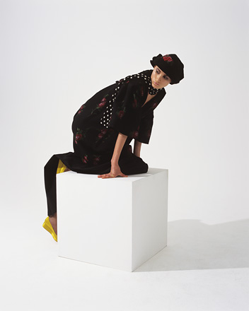 Woman crawling on top of a white cube, facing the left