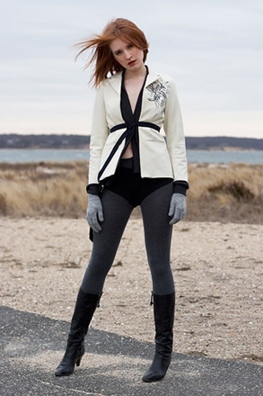 A woman wearing a white jacket, dark dray leggings, and black calf-high boots on a beach in winter