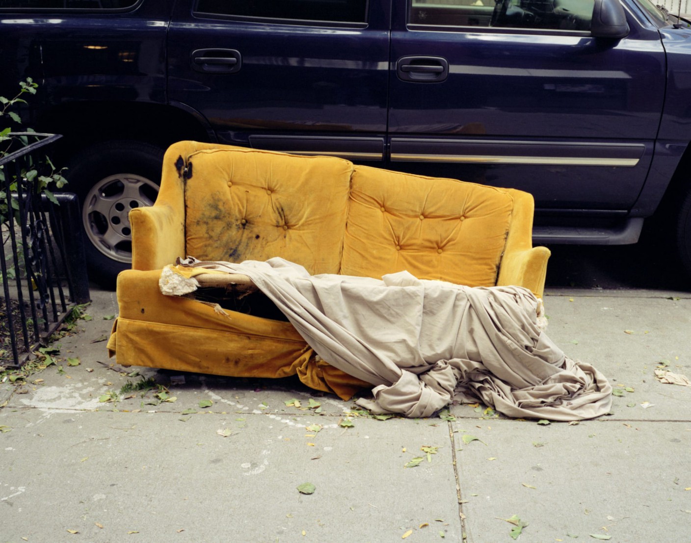 A discarded yellow couch with a white blanket, on a sidewalk
