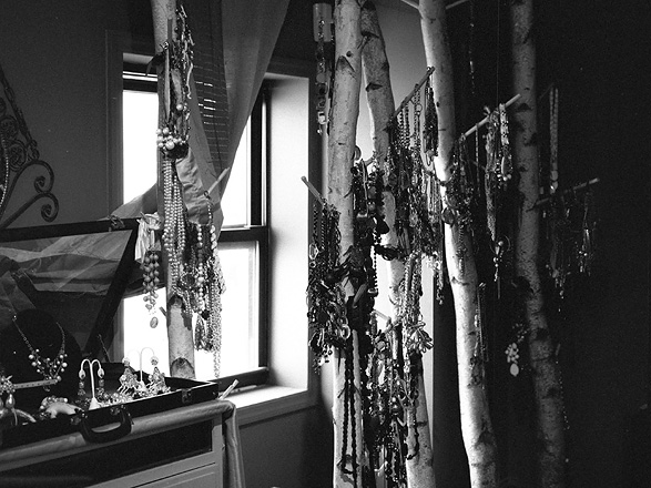 Jewelry hanging on small, white tree trunks inside a room