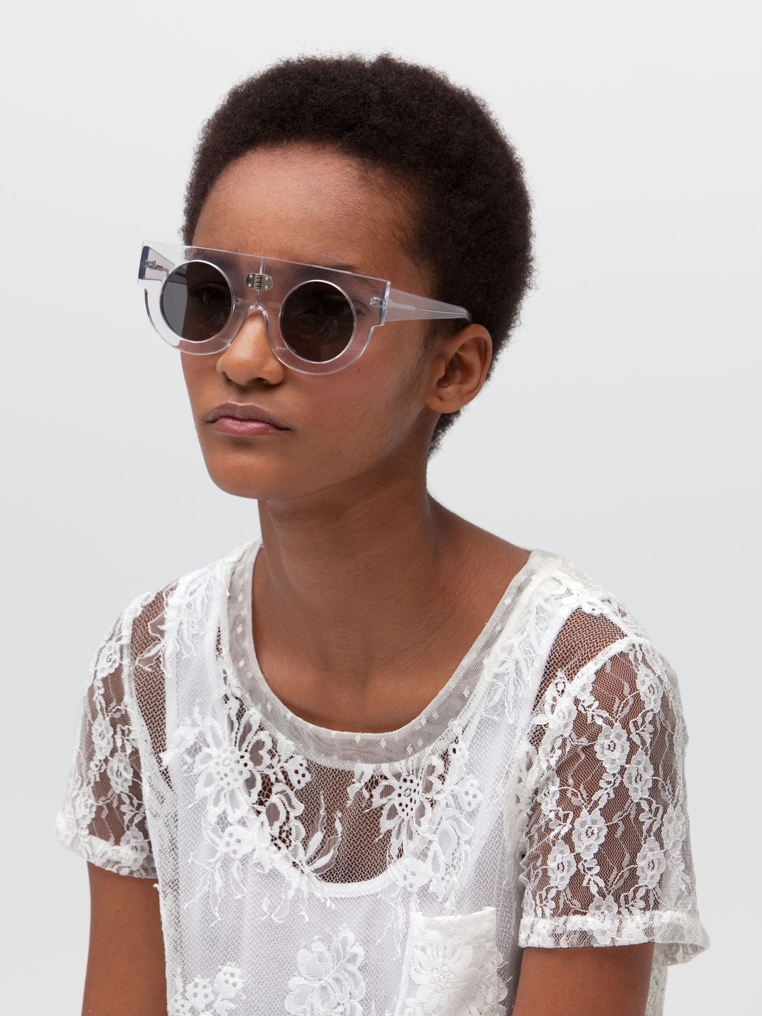Woman wearing a see-through white lace top with white tanktop underneath and transparent-framed sunglasses with dark round lenses