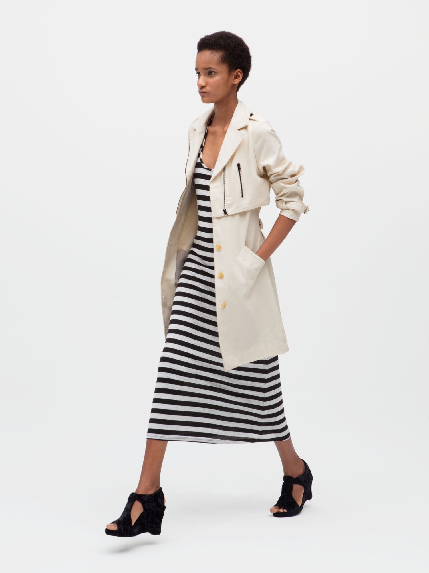 Woman wearing a long striped black-and-white dress with white trench coat rolled up at the sleeves